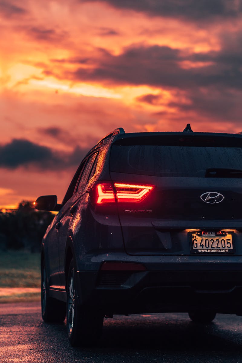 Rear view of a modern Hyundai SUV on a wet road during a vibrant sunset, showcasing dramatic cloudscape.